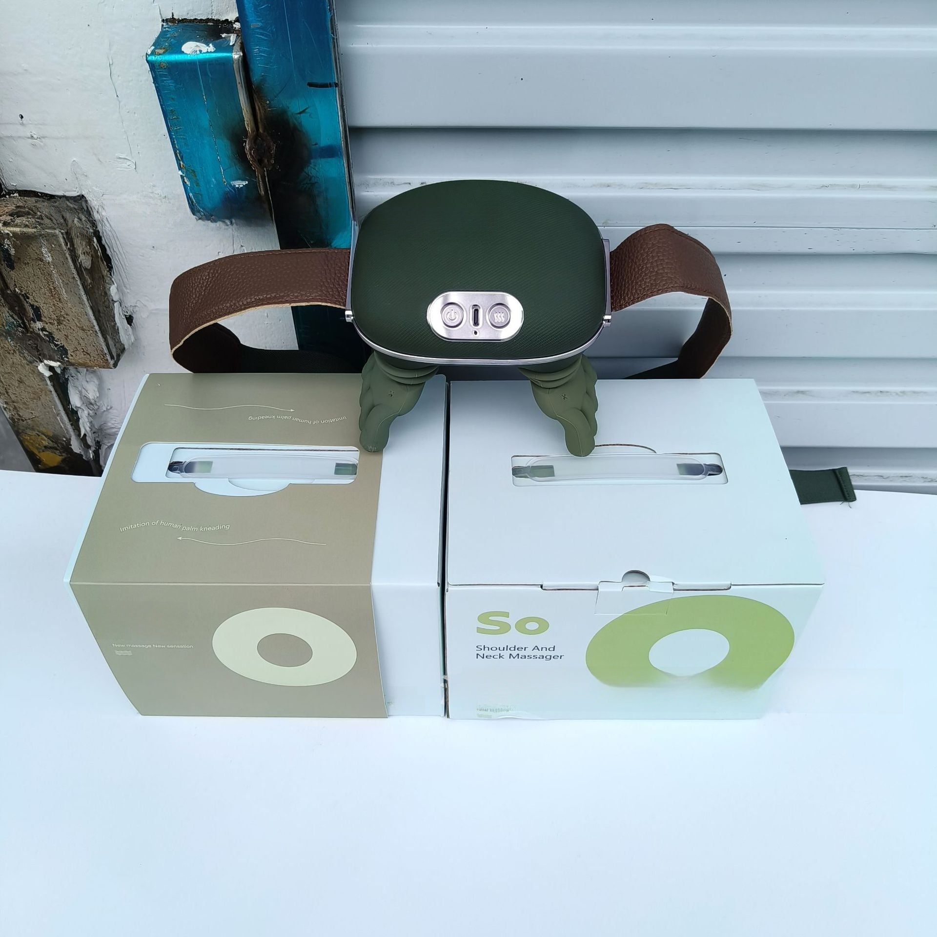 Green neck massager on top of two boxes with visible branding against a white wall.